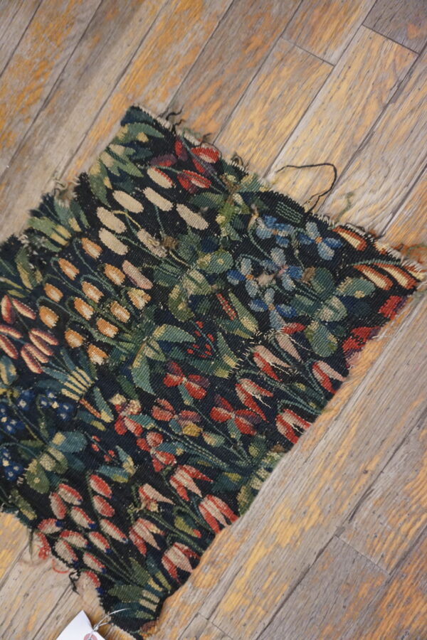 A frayed flatweave rug remnant with a dark floral pattern rests on distressed wooden floorboards.