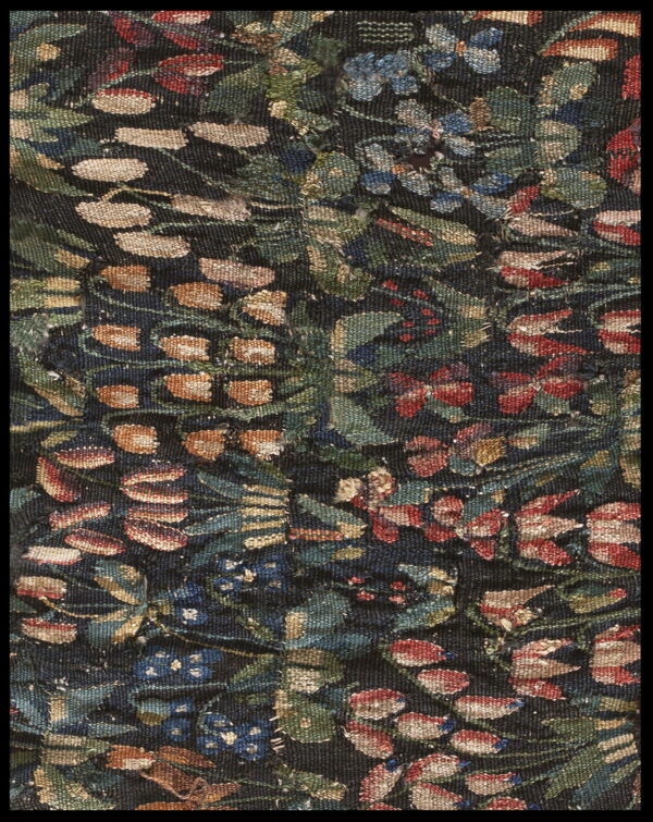 Woven detail of a rug with dense floral tapestry pattern in green, blue, rust, and cream colors.