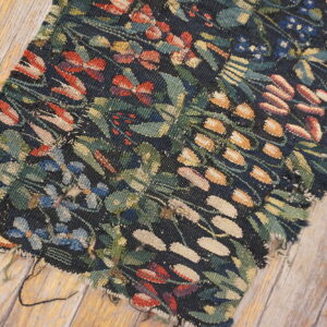 Dark flatweave rug fragment with red, green, and gold botanical designs resting on weathered wood planks.