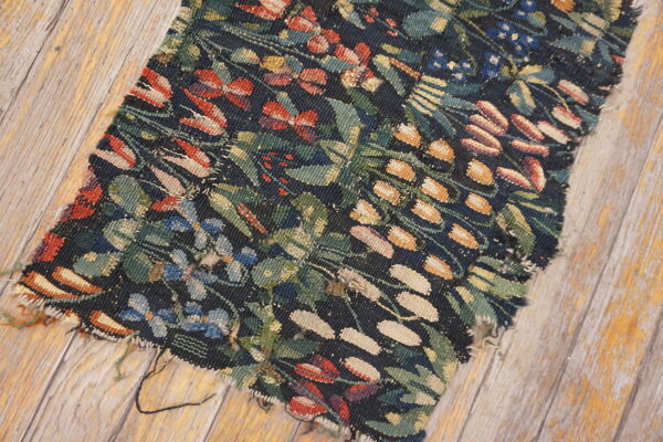 Dark flatweave rug fragment with red, green, and gold botanical designs resting on weathered wood planks.