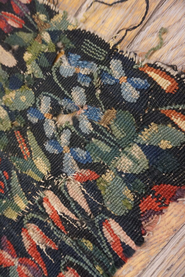 Heavily textured, dark floral rug fragment with blue, green, and red motifs sits on wooden flooring.