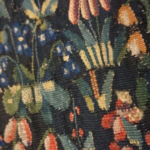 Tight close-up of a low-pile floral rug showing dark blue ground, red, gold, and green woven details.
