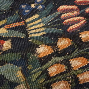 Flatweave textile fragment features a floral pattern with orange, red, and green woven details on a dark background.