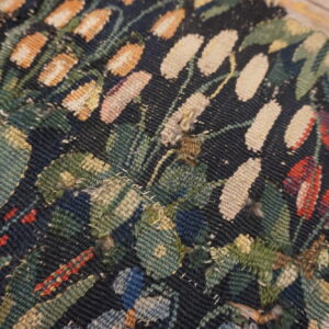 Close view of a dark flatweave textile with woven floral patterns in green, beige, red, and orange resting on wood.