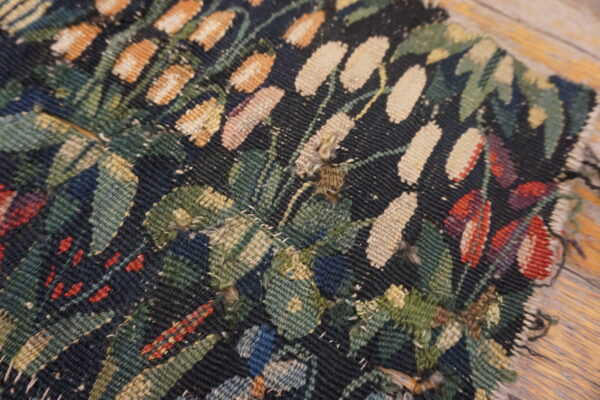 Close view of a dark flatweave textile with woven floral patterns in green, beige, red, and orange resting on wood.