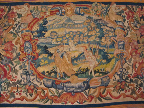 Flat-woven rug features a central pastoral scene surrounded by an ornate border with florals and stylized masks.