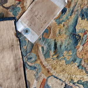 A textured blue, gold, and rust tapestry corner is folded, revealing striped backing and an attached label.