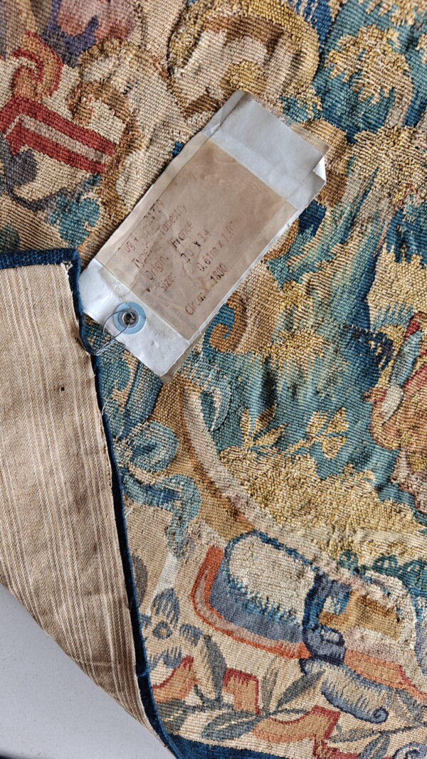 A textured blue, gold, and rust tapestry corner is folded, revealing striped backing and an attached label.