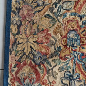 Woven rug detail showing dense, textured botanical patterns in red, gold, and blue on a pale ground.