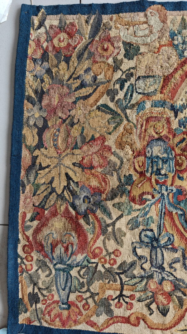 Woven rug detail showing dense, textured botanical patterns in red, gold, and blue on a pale ground.