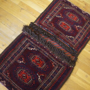 A small red and blue geometric rug, joined in the center by thick brown looped fringe, rests on wood planks.