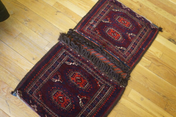 A small red and blue geometric rug, joined in the center by thick brown looped fringe, rests on wood planks.