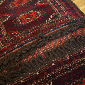 Close-up of a burgundy and red geometric rug featuring thick dark braided tassels on wood flooring.
