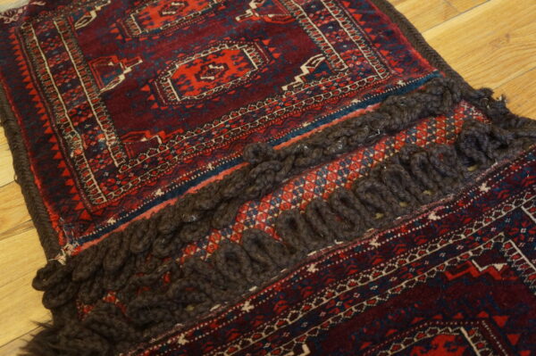 Close-up of a burgundy and red geometric rug featuring thick dark braided tassels on wood flooring.