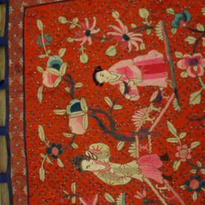 Close-up of a red textile featuring detailed embroidery of figures, pink and blue flowers, and a silver beaded lattice.