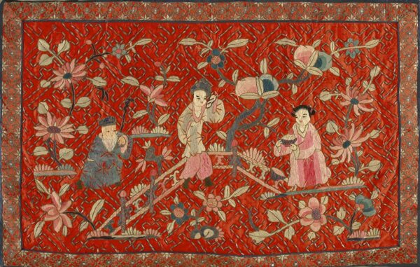 Vibrant red embroidered textile featuring three figures, detailed pink and blue flowers, and a complex scrolled border.