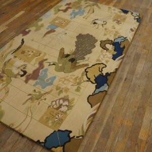 A low pile tan rug with an elaborate peacock and bird pattern lies on distressed wood flooring.