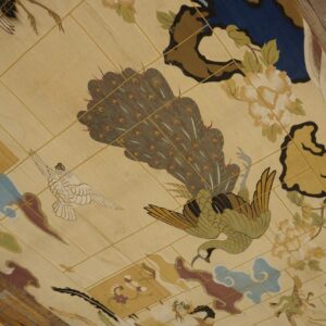 Cream rug with a detailed avian and floral design in green, brown, blue, and burgundy on distressed wood floor.