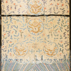 Cream embroidered textile displaying central gold dragon motifs, blue cloud scrolls, and a border of multicolored diagonal stripes.