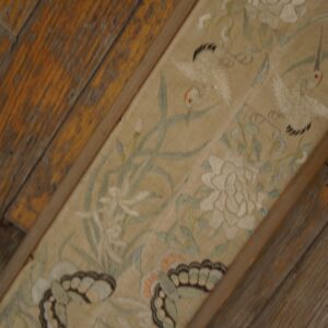 Detailed beige rug strip featuring white floral, crane, and butterfly motifs, bordered by aged wooden planks.