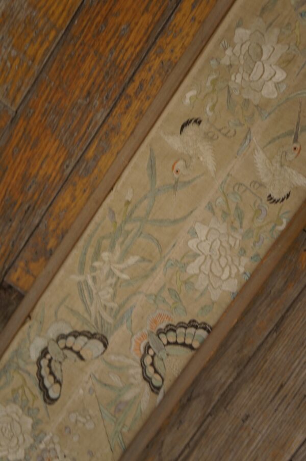 Detailed beige rug strip featuring white floral, crane, and butterfly motifs, bordered by aged wooden planks.