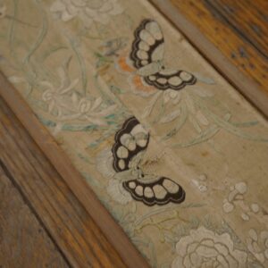 Close-up of a pale embroidered floral and butterfly runner resting on distressed wood floor planks.