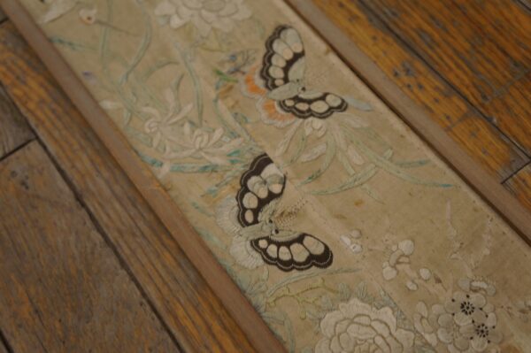 Close-up of a pale embroidered floral and butterfly runner resting on distressed wood floor planks.