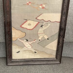 Framed gray and tan low-pile textile featuring two stylized figures and a dark carved frame.