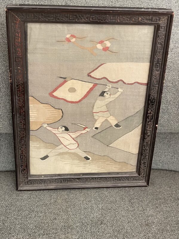 Framed gray and tan low-pile textile featuring two stylized figures and a dark carved frame.