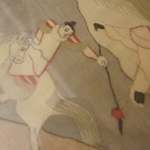 Figurative rug detail features beige horses and a rider in red and white stripes on a taupe background.