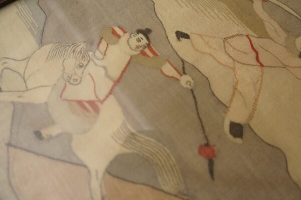 Figurative rug detail features beige horses and a rider in red and white stripes on a taupe background.