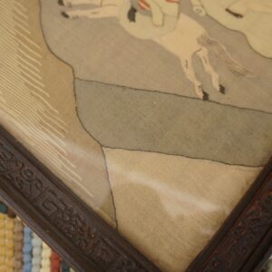 A detailed framed artwork rests on a striped, high-pile rug with teal, yellow, and white bobbles.