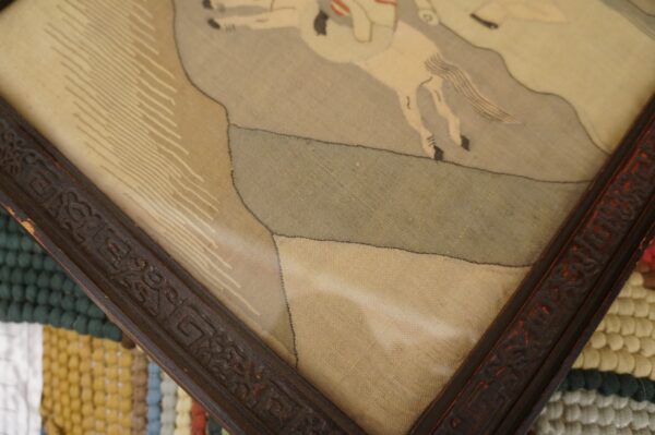 A detailed framed artwork rests on a striped, high-pile rug with teal, yellow, and white bobbles.