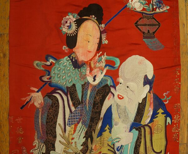 Flatweave textile in bright red with a detailed multi-color figural pattern on light brown wood flooring.