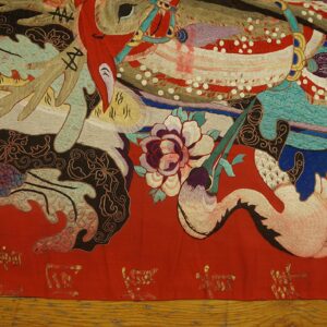 Textured textile featuring complex figures and flowers in red, teal, black, and white on a wood floor.