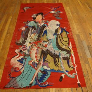 A long, red embroidered rug featuring multicolored figures, animals, and script lies on wooden floors.