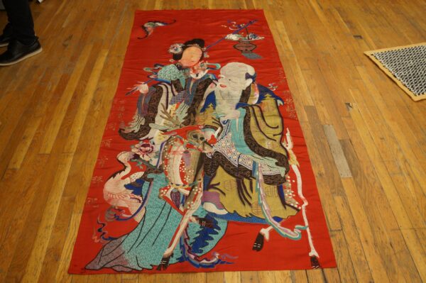 A long, red embroidered rug featuring multicolored figures, animals, and script lies on wooden floors.