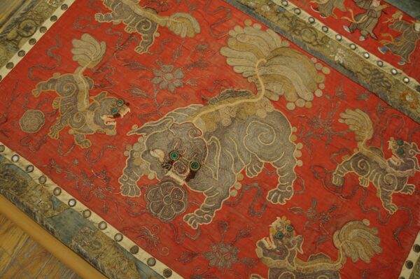 Detailed red textile featuring embroidered gray and tan mythical beasts with prominent teal eyes.