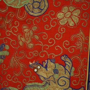 Red rug with metallic gold scrollwork, blue and green mythical motifs, and a dark blue key border.