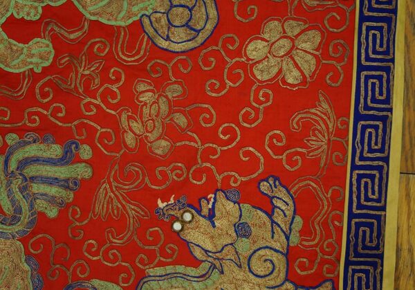 Red rug with metallic gold scrollwork, blue and green mythical motifs, and a dark blue key border.