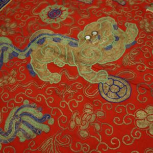 Red rug with detailed metallic gold, blue, and green embroidery depicting a central mythical lion motif.