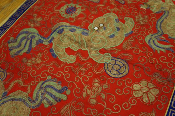Red rug with detailed metallic gold, blue, and green embroidery depicting a central mythical lion motif.