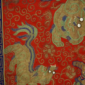 Red embroidered textile featuring gold, teal, and blue mythical figures and a meander border.