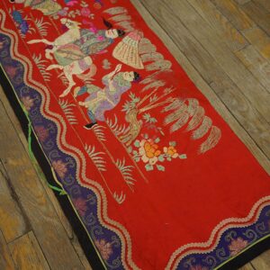 Flat red runner with embroidered figures and a purple border rests on worn wooden floorboards.