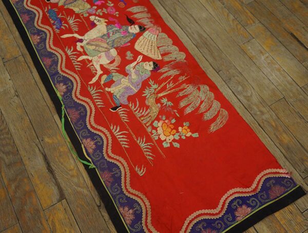 Flat red runner with embroidered figures and a purple border rests on worn wooden floorboards.