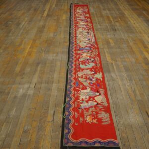 Long red textile runner with colorful embroidered figures on a distressed wooden plank floor.