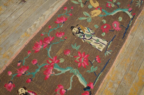Figurative textile runner with magenta and teal floral embroidery lies on distressed gray wood flooring.