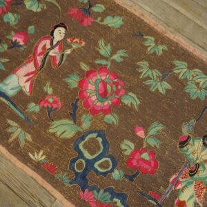 Dark brown low-pile rug featuring colorful figures, pink florals, and green leaves on wood floor.