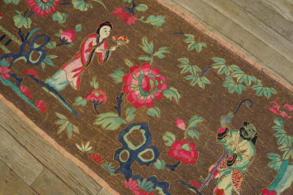 Dark brown low-pile rug featuring colorful figures, pink florals, and green leaves on wood floor.