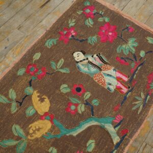 Brown embroidered rug featuring a stylized person, magenta flowers, and green leaves on rustic wooden floorboards.